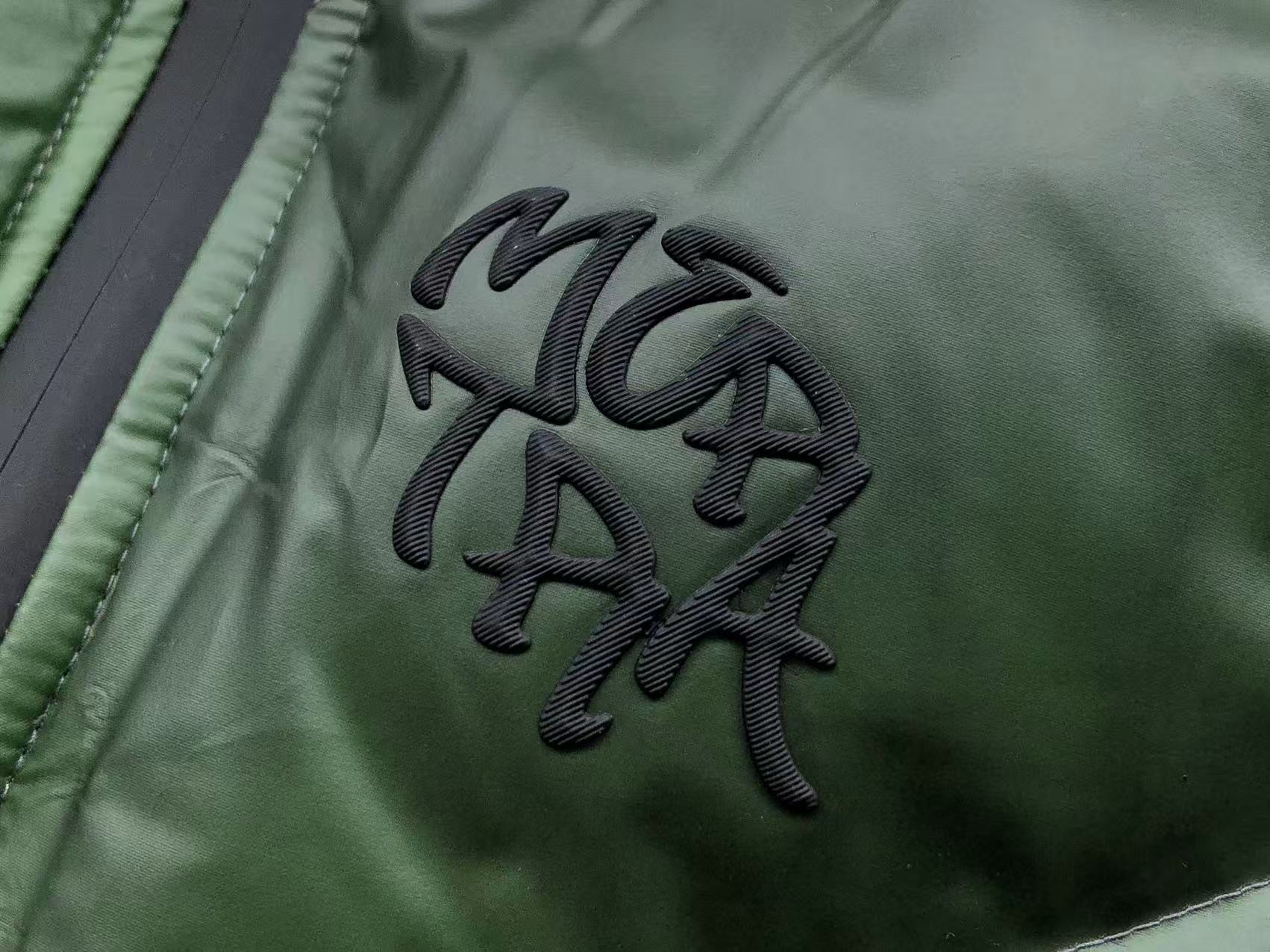 Close-up of a green jacket with a black embroidered logo on a dark background
